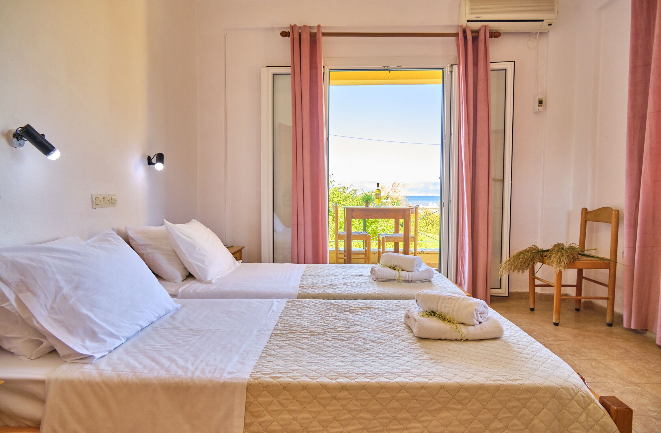 Ein Hotelzimmer mit zwei Betten, einem Balkon mit einem Stuhl und Meerblick.