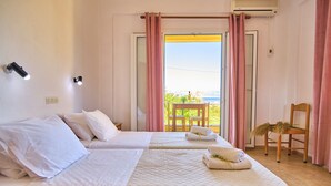 A hotel room with two beds, a balcony with a chair, and a view of the sea.