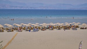 A beach with rows of sun loungers and umbrellas, a clear sky, and a calm sea.
