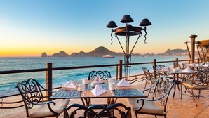An outdoor dining area with tables and chairs, overlooking a body of water and distant mountains.