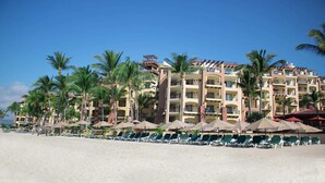 A beachfront hotel with multiple balconies, palm trees, and rows of sun loungers.