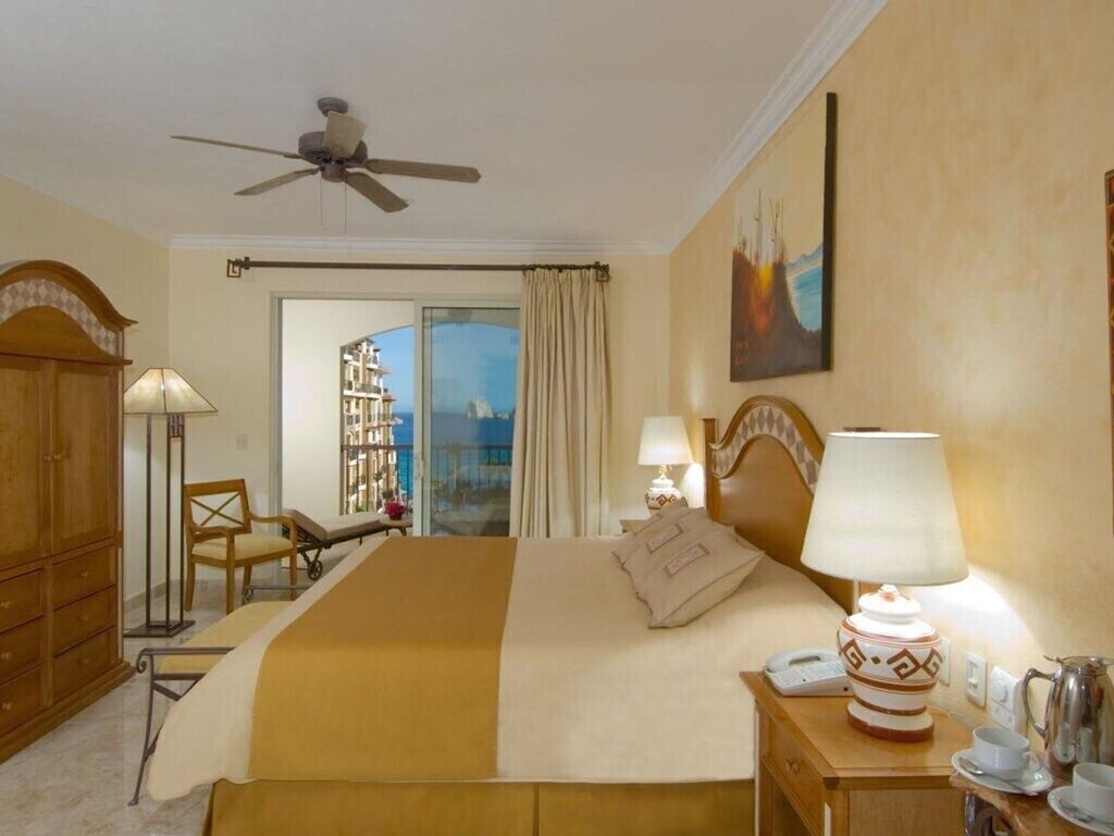 A hotel room with a bed, bedside table, lamp, and a view of the sea through a large window.