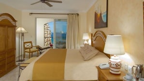 A hotel room with a bed, bedside table, lamp, and a view of the sea through a large window.