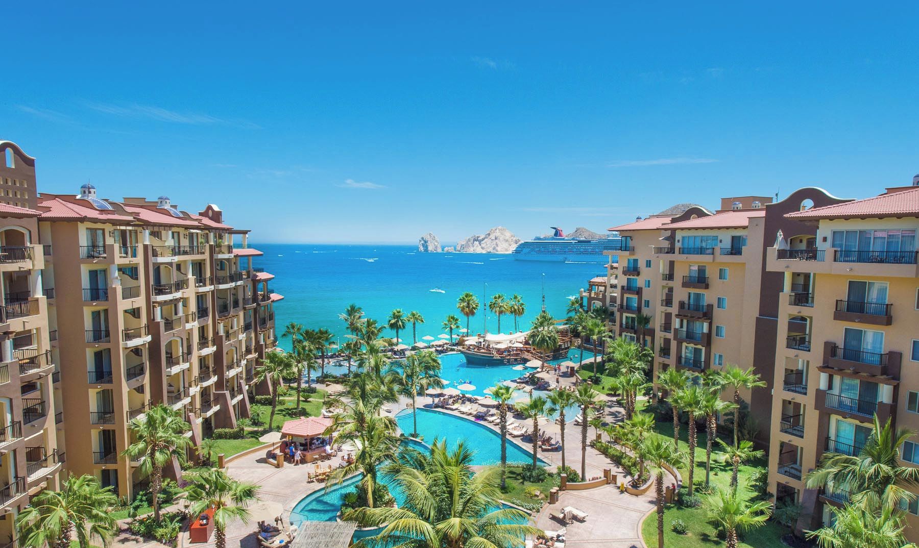 Ein Resort mit mehreren Gebäuden, einem zentralen Poolbereich und Blick auf den Ozean.