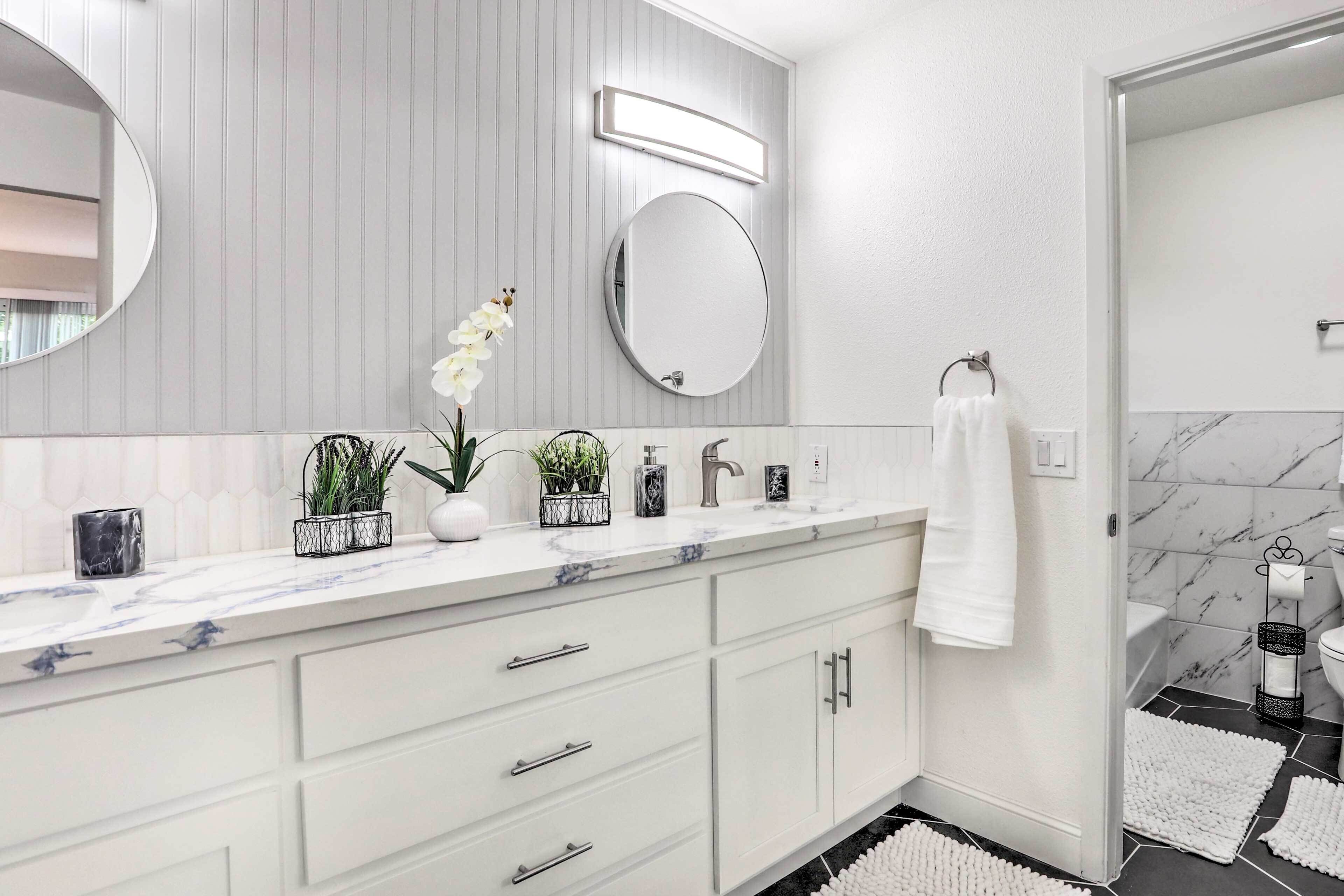 A modern bathroom with a white vanity, two mirrors, a marble countertop, and a black and white tiled floor.