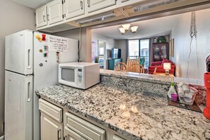 Kitchen area with refrigerator, microwave, and dining space leading to a room with a large window and outside view.