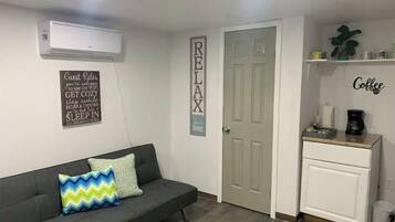 Ein modernes Wohnzimmer mit einem grauen Sofa, einer Kaffeestation und einer Tür mit der Aufschrift 'RELAX'.