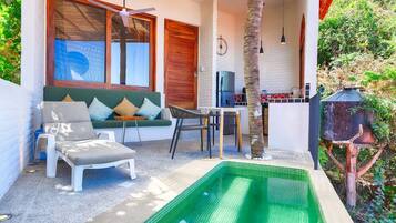 A pool area with a green pool, a sofa with cushions, a table, and a chair.
