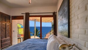 Een slaapkamer met een groot bed, uitzicht op de oceaan en een balkon met een houten deur.