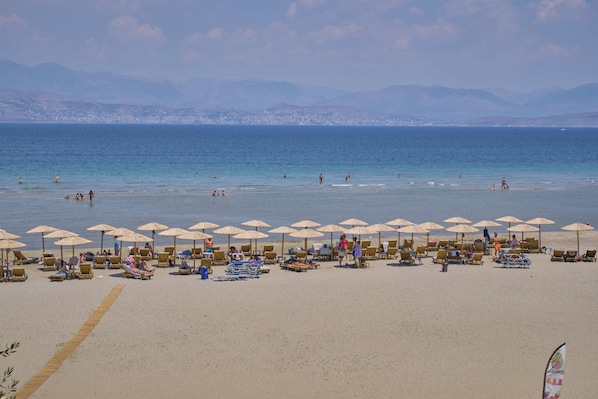 A beach with sun loungers and umbrellas, a clear sky, and a distant cityscape.