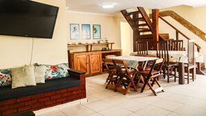 Un coin repas avec une table et des chaises en bois, un canapé en briques, un téléviseur fixé au mur et un escalier menant à un autre niveau.