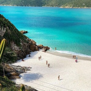 A beach with clear turquoise water, rocky outcrops, and people enjoying the sand. - CASA MARAVILHOSA 6 QUARTOS (Arraial do Cabo)