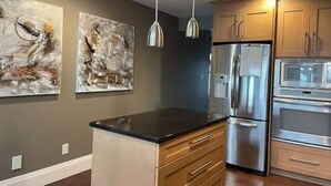 A modern kitchen with stainless steel appliances, wooden cabinets, and abstract wall art. - The Lakeside House With Hot Tub! (Amherstburg)