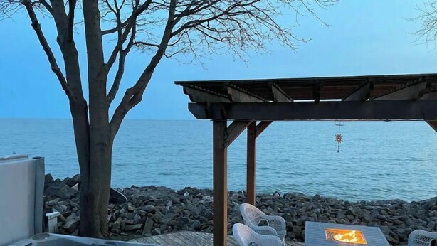 A hot tub, outdoor seating, and a pergola overlooking a body of water. - The Lakeside House With Hot Tub! (Amherstburg)