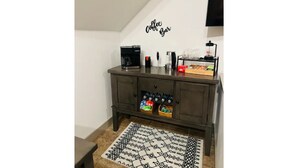 Ein kleiner Bereich mit einer Kaffeebar, einer Kaffeemaschine, Tassen und einer Kaffeemühle auf einem dunklen Holzschrank.