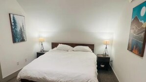 Ein Schlafzimmer mit einem großen Bett, zwei Nachttischen mit Lampen und zwei an der Wand hängenden Bildern.