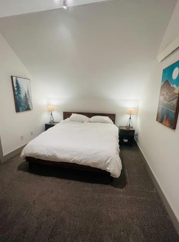 A bedroom with a large bed, two bedside tables with lamps, and two wall-mounted paintings. - Westside Bozeman Nook - Cozy Destination (Bozeman)