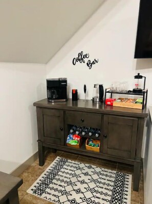 Un pequeño espacio de cafetería con una máquina de café, tazas y un molinillo sobre un mueble de madera oscura.