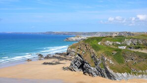 A coastal landscape with a sandy beach, rocky cliffs, and a clear blue sky. - Spacious apartment, breathtaking sea views, private secure parking. (Newquay)
