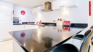 A modern kitchen with white cabinets, stainless steel appliances, a large island, and a red clock on the wall. - Spacious apartment, breathtaking sea views, private secure parking. (Newquay)