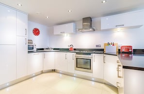 A modern kitchen with white cabinetry, a stainless steel oven, a red clock, and a red toaster.