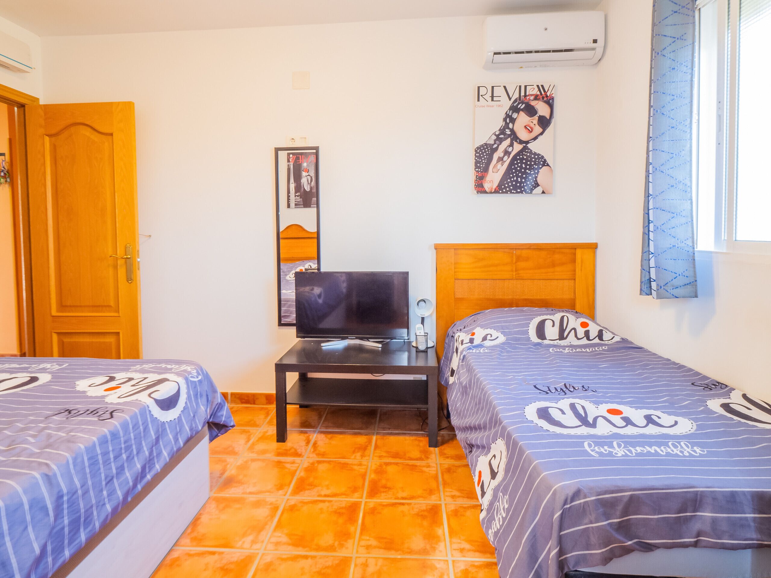 A hotel room with two beds, a TV, a small table, and a poster on the wall.