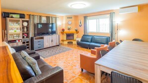 Ein Wohnzimmer mit Fernseher, einer Couch, einem Esstisch und Stühlen.