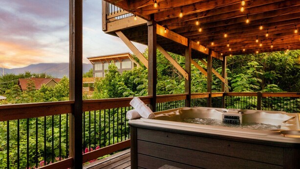Een hottub op een houten terras met uitzicht op een weelderige tuin en bergen op de achtergrond.