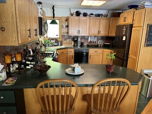 A kitchen with wooden cabinets, a black refrigerator, a stove, and two wooden chairs. - Waterfront retreat on 7 private wooded acres with beautiful sunset views. (Aurora)