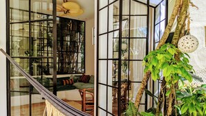 A hammock in a room with a glass partition, a ceiling fan, and a large window overlooking a lush garden. - Designer's Villa At Playacar Beach (Playa del Carmen)