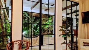 A room with large glass doors leading to a garden, a wicker chair, a potted plant, and a sofa. - Designer's Villa At Playacar Beach (Playa del Carmen)