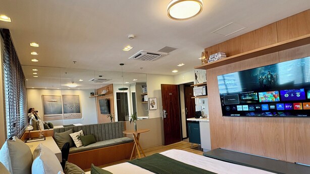 Una habitación de hotel moderna con una cama grande, un sofá, un televisor montado en la pared y una pequeña kitchenette.