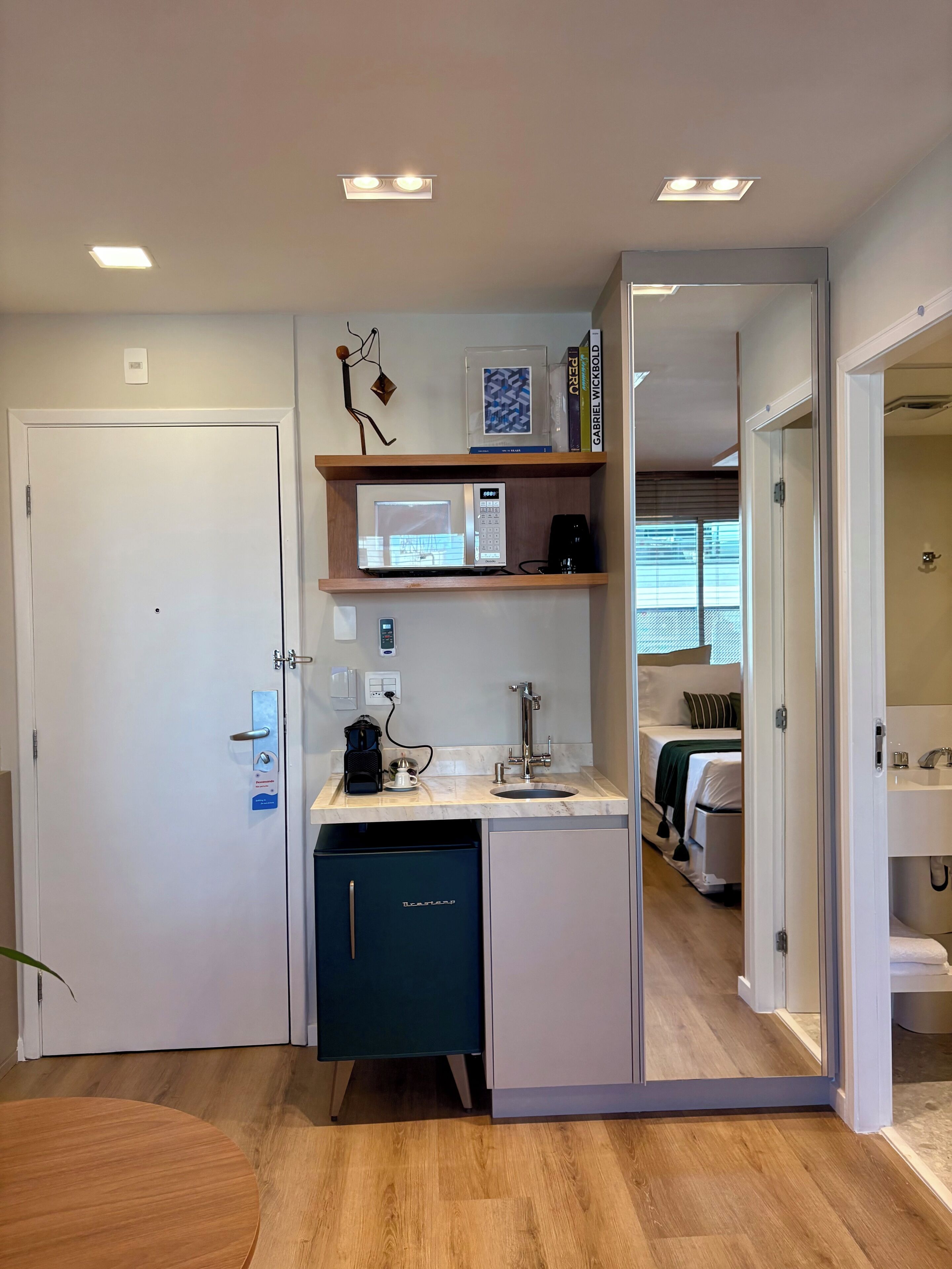 A compact kitchenette with a microwave, coffee maker, and sink. A small cabinet and a door with a handle are also visible.