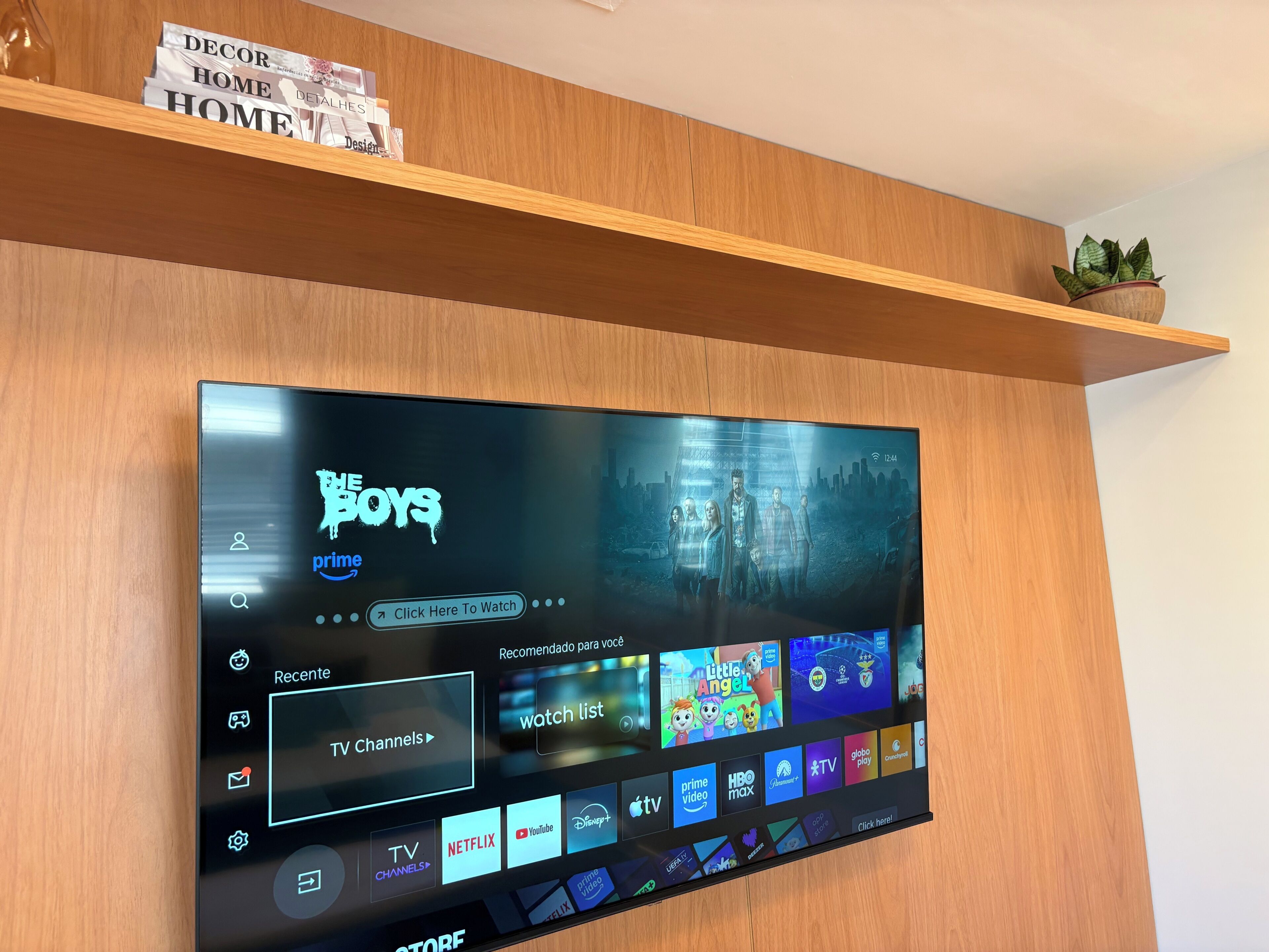Televisor de pantalla plana instalado en una pared de madera, mostrando una interfaz de transmisión con varios iconos de aplicaciones y la opción 'TV Channels'.