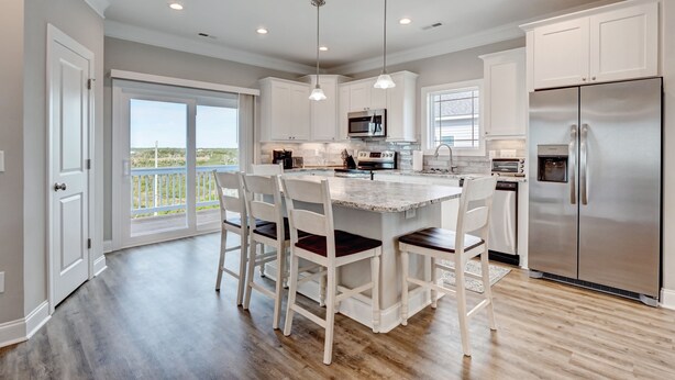 Una cocina moderna con armarios blancos, una isla central con taburetes de bar, un refrigerador de acero inoxidable y un ventanal con vistas.