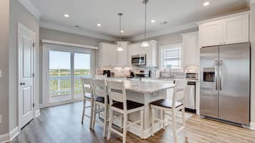 A modern kitchen with white cabinetry, a central island with bar stools, a stainless steel refrigerator, and a large window offering a view.