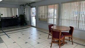 Un comedor con una mesa redonda de madera y sillas rojas, una cocina con encimera negra y ventanas amplias con persianas verticales.