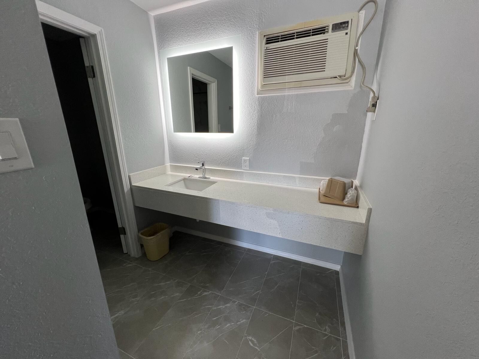 A bathroom with a white sink, a mirror, and a wall-mounted air conditioner.