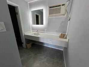 A bathroom with a white sink, a mirror, and a wall-mounted air conditioner.