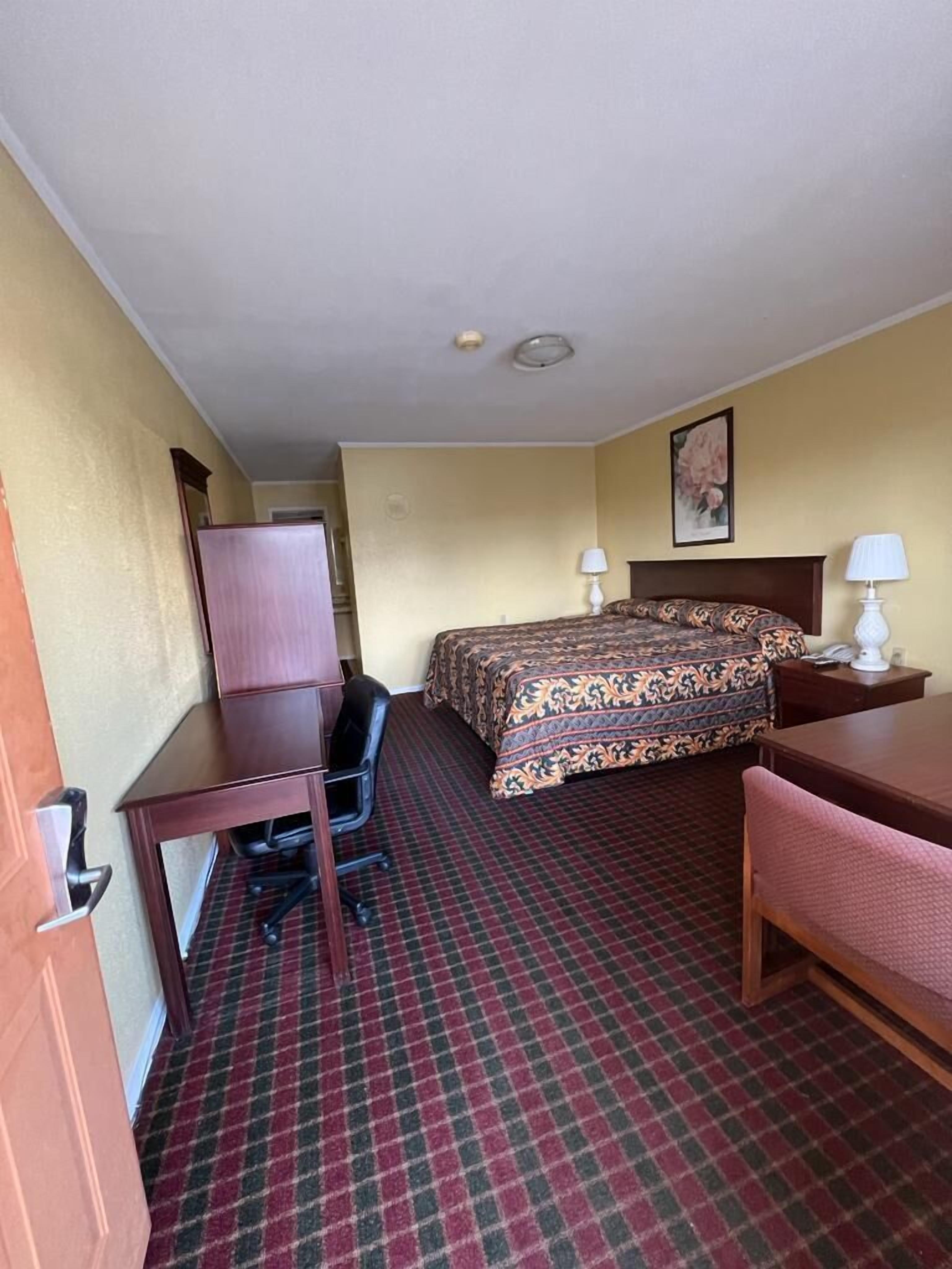 A hotel room with a bed, desk, chair, and a small table.