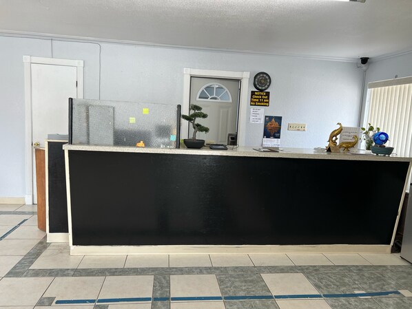 A reception desk with a black counter, a clock, a notice board, and a potted plant.
