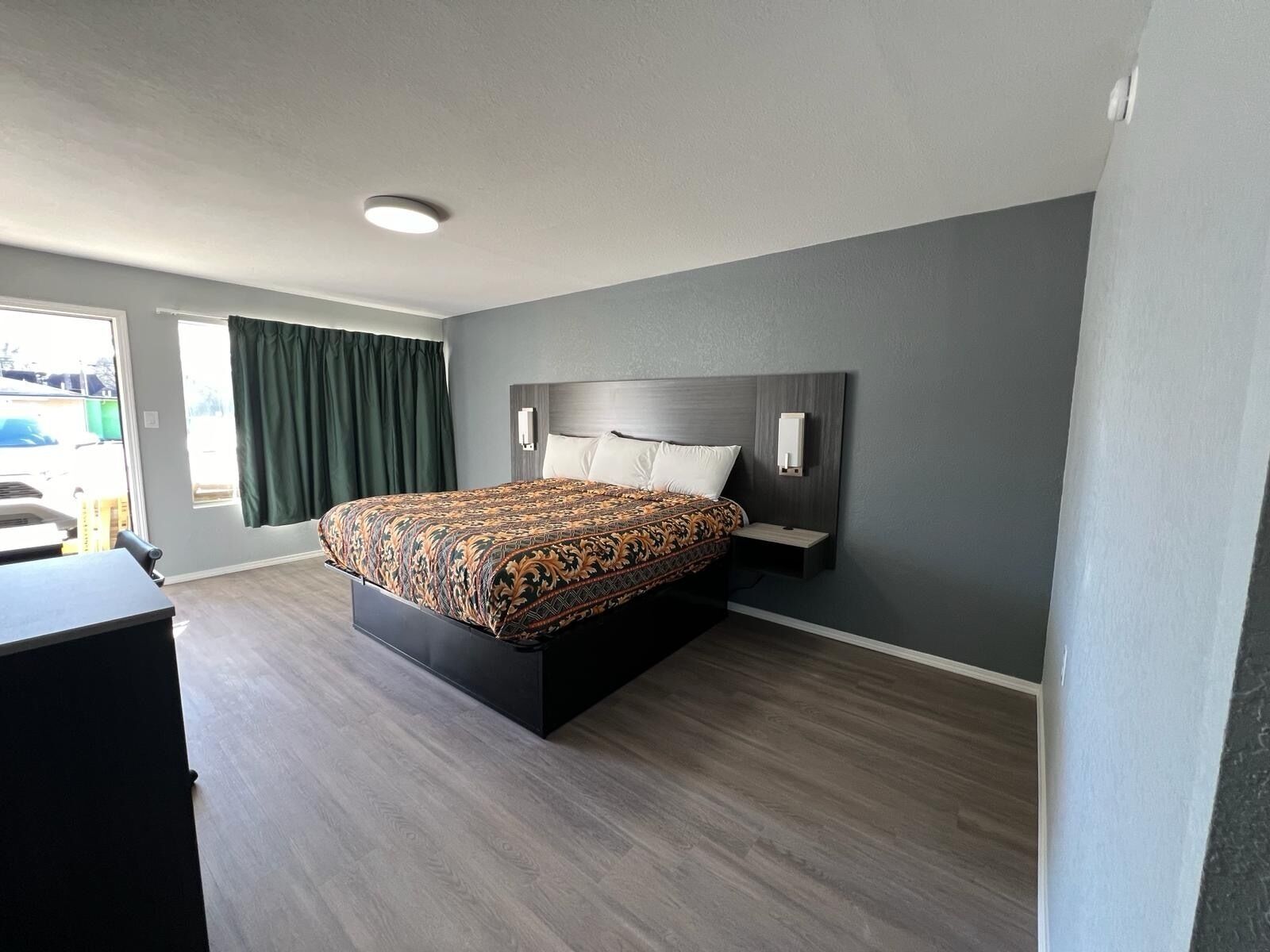 Una habitación de hotel moderna con una cama grande, un escritorio y un ventanal con cortinas.