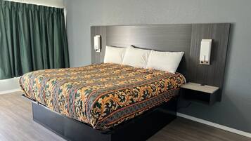 Una habitación de hotel moderna con una cama grande, piso de madera oscura, paredes grises y una cortina verde.