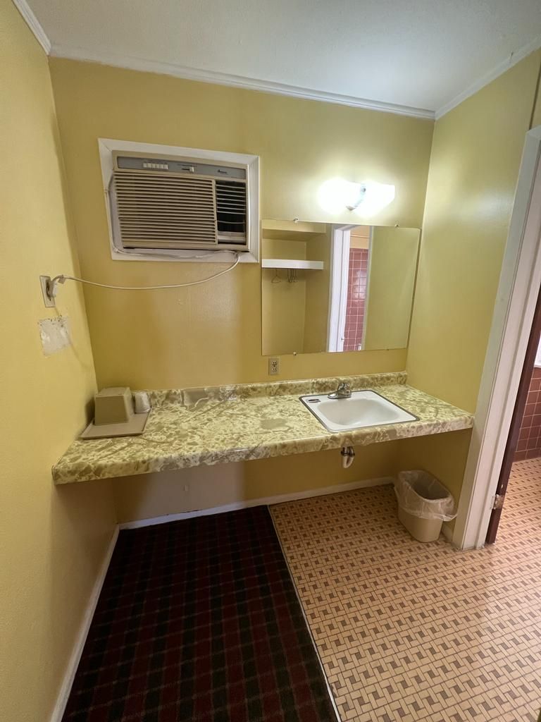 A bathroom with a single sink, a mirror, and a wall-mounted air conditioner.