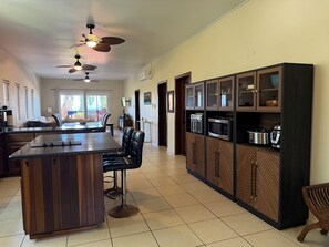 A kitchen with a central island, bar stools, a microwave, oven, and a built-in cabinet with glass doors. - Large 2-bedroom condo West End with stunning views and close to beach (West End)