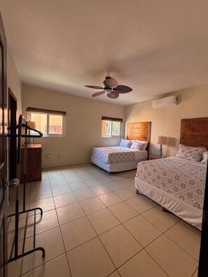 A bedroom with two beds, a ceiling fan, an air conditioning unit, and a window. - Large 2-bedroom condo West End with stunning views and close to beach (West End)