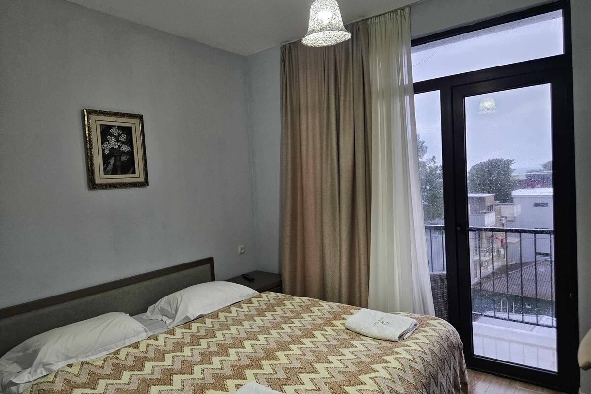 Habitación de hotel con cama, un cuadro en la pared, ventana con cortinas y vistas al exterior.