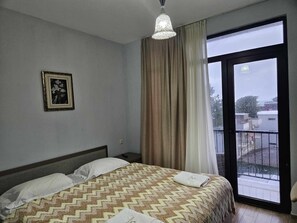 Ein Hotelzimmer mit Bett, einem gerahmten Bild an der Wand, einem Fenster mit Vorhängen und Blick nach draußen.