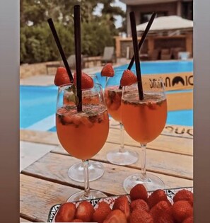 Zwei Cocktails mit Erdbeeren und schwarzen Strohhalmen, ein Pool und ein Holztisch mit weiteren Erdbeeren.