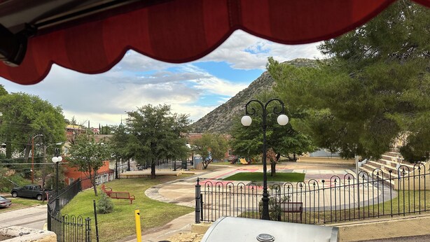 Blick von einer überdachten Außenbereich mit Grill, umzäuntem Spielplatz und Berg im Hintergrund.
